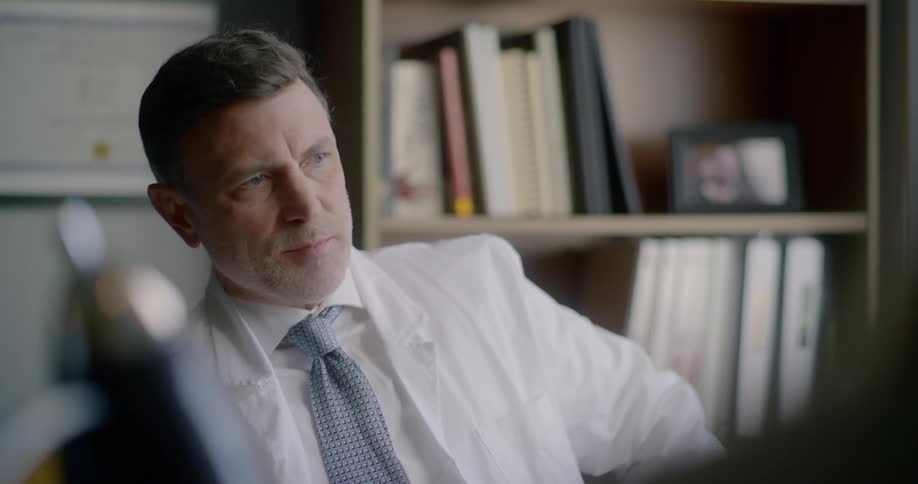 A man with a shirt and tie sitting down in an office talking