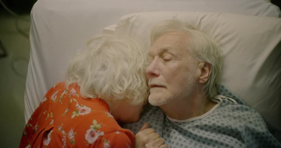 Elderly wife hugs her husband who lies on hospital bed