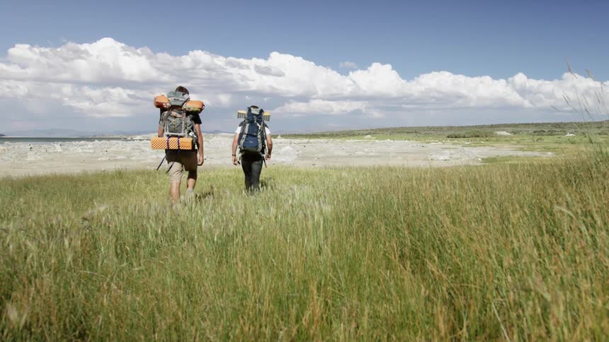 Two guys backpacking through a field