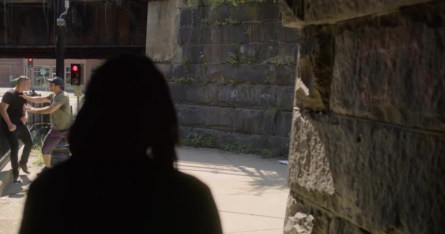 Mans silhouette walks down the alley and stops to look at the people fighting each other on the street