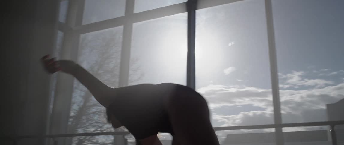 A woman dances before a large sunny window