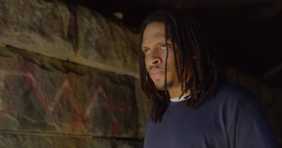 A man stands under a bridge and stares angrily into the distance