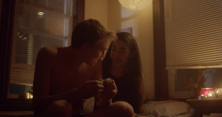 Two teenagers sit on a bed and talk
