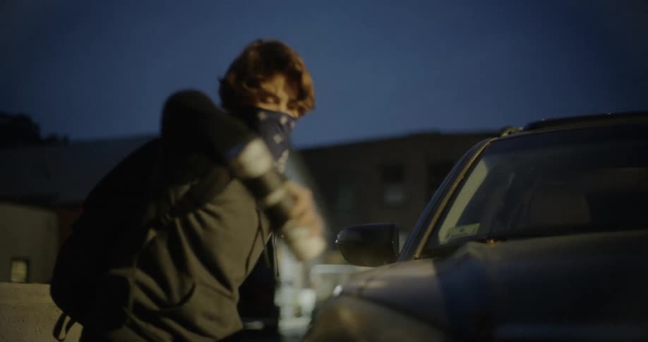 A teenager spray paints and vandalizes a parked car