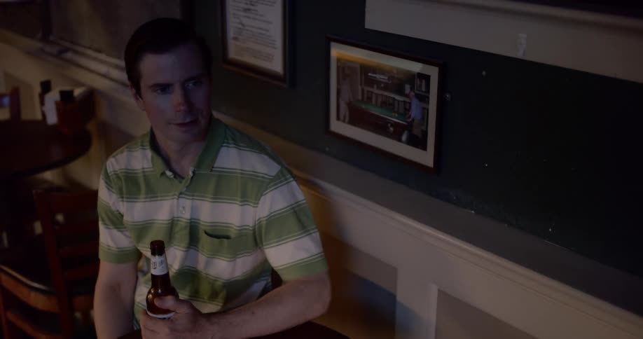 A man sitting at a table in a dimly lit bar holding a bottle of beer