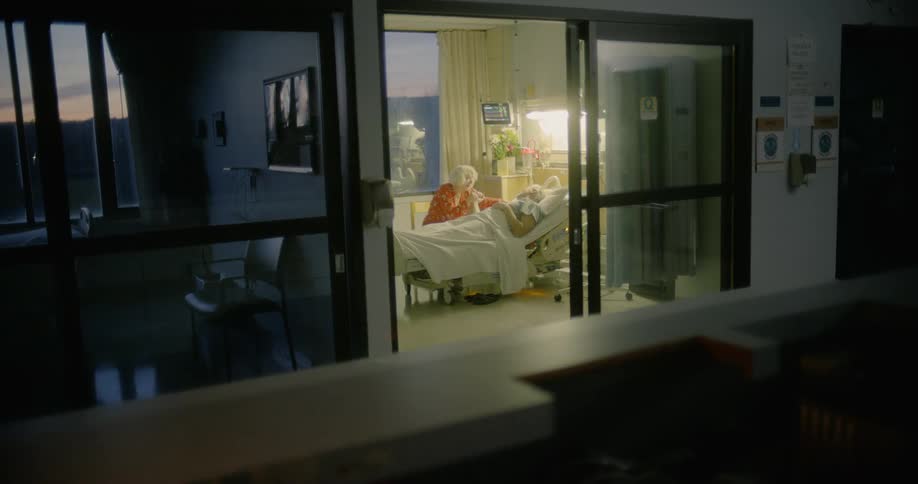 A woman sits by a mans hospital bed