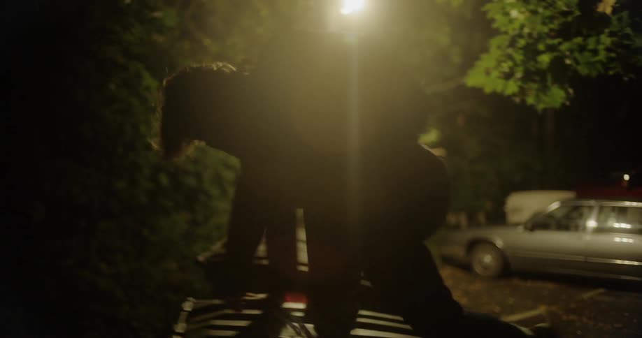 A person running through a parking lot at night and vaulting over a dumpster