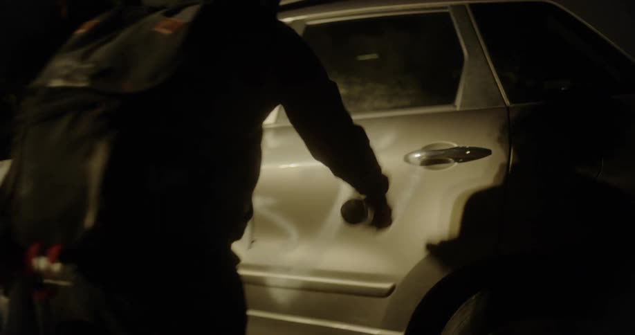 A teenager spray paints graffiti on the side of a vehicle at night