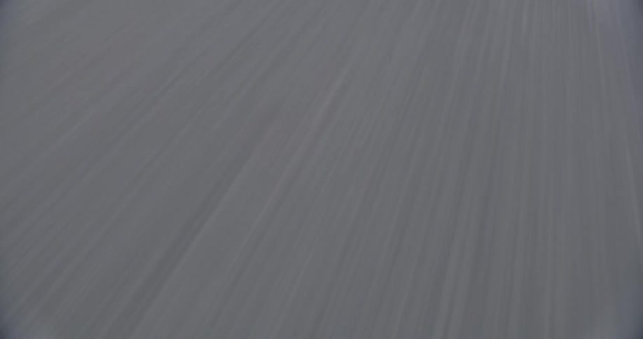 The asphalt blurs into gray lines as it is traveled on and sunlight and shadows become visible as the movement slows