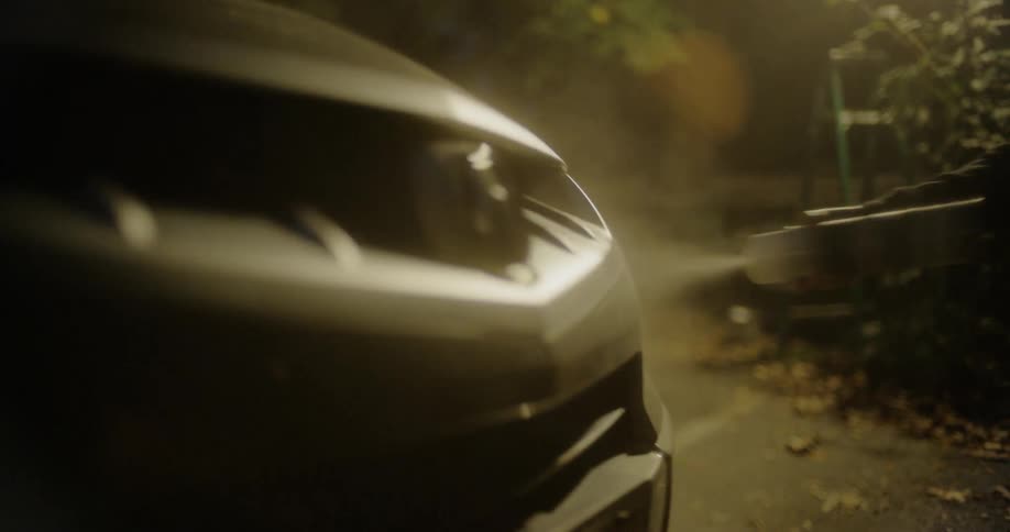 A person with a bandanna over their face vandalizing a vehicle with spray paint in a parking lot at night