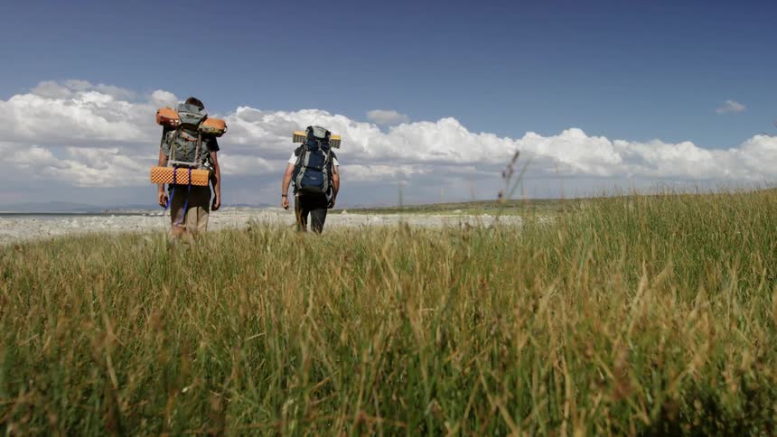 Two men hike across a grass field on a sunny day