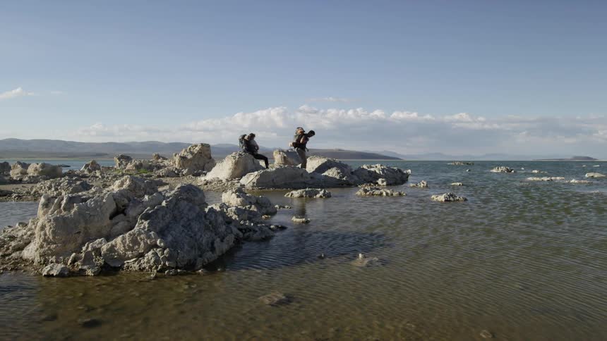 Hikers walking over rocks to stand on boulders in very shallow water