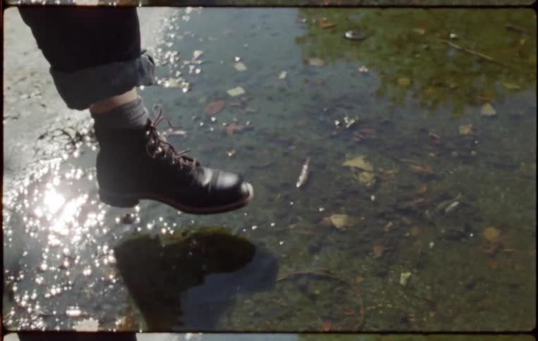 A persons foot with boots stomping on a puddle of water