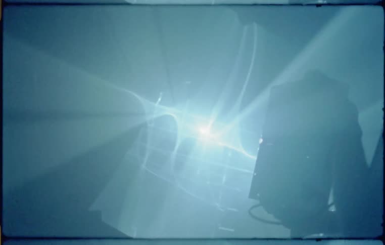 A person in a dark room holding a projector that is giving off light