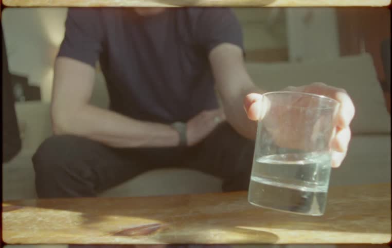 A man sits on a couch holding a glass of water