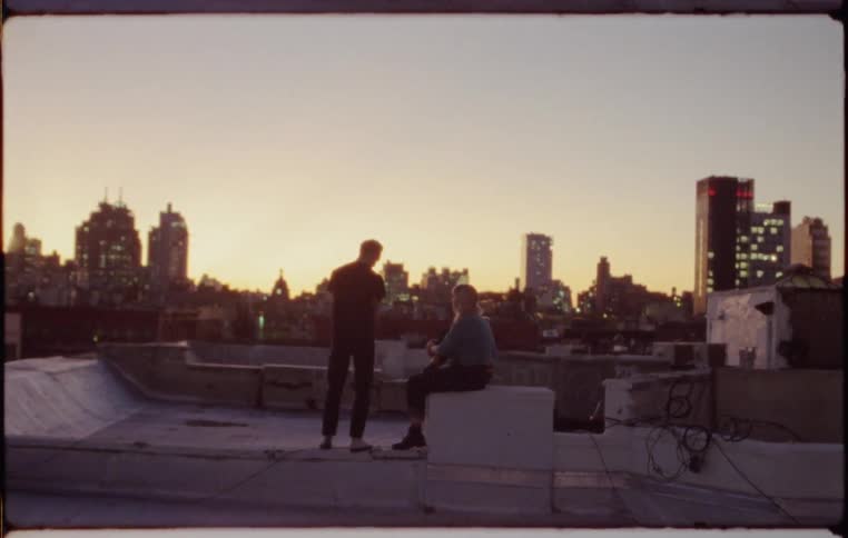 A man and a woman on a rooftop with the city skyline in the background