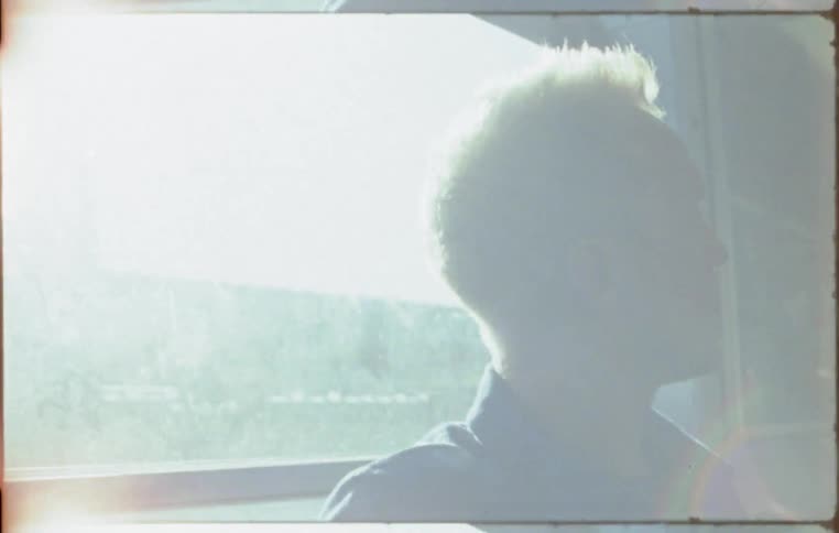 The sun shines through the window of a train behind a passenger