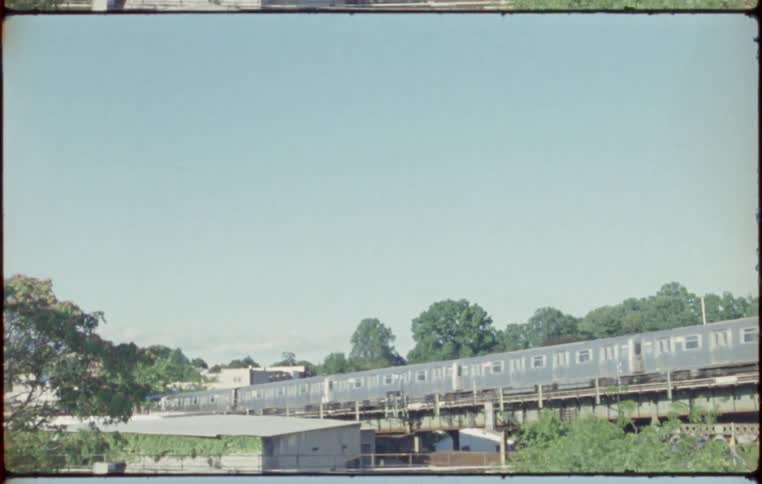 A long thin train travels along metal tracks and carries people to the station
