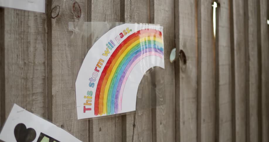 A wooden fence with childrens drawings on paper on it