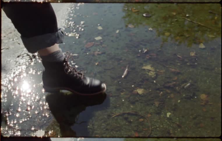 Person touches puddle with foot shod in half boots