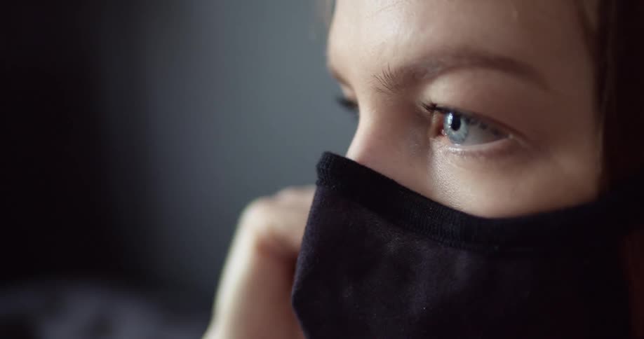 Blue eyed woman wears a black face mask and looks a head