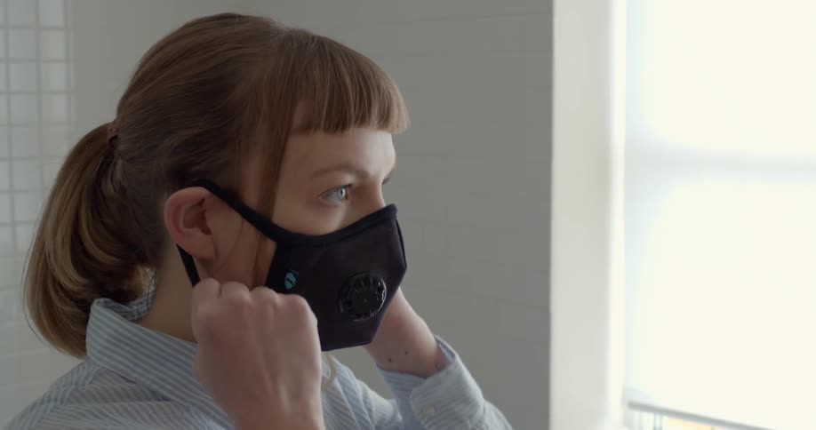 A woman puts on a cloth face mask with a filter over her nose and mouth