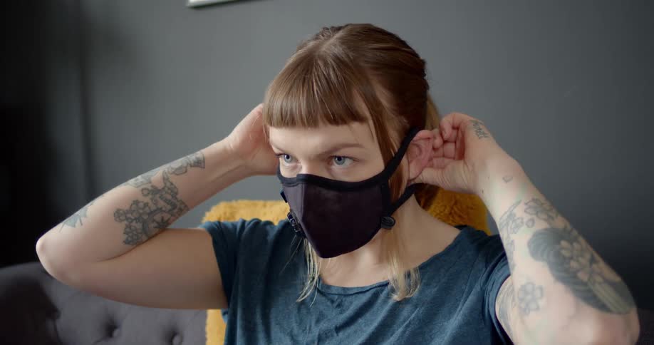 A woman putting on a filter mask while sitting on a sofa