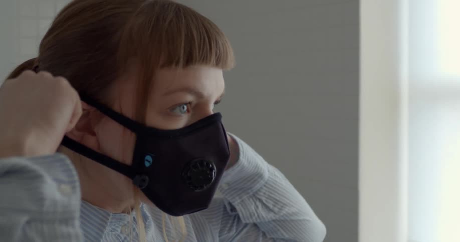 A woman is putting on a mask indoors