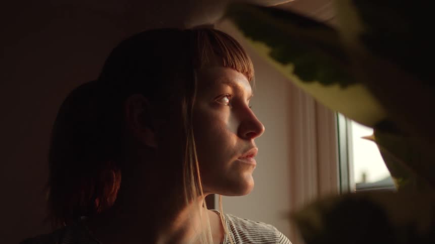 A woman sits and looks out a window in her apartment