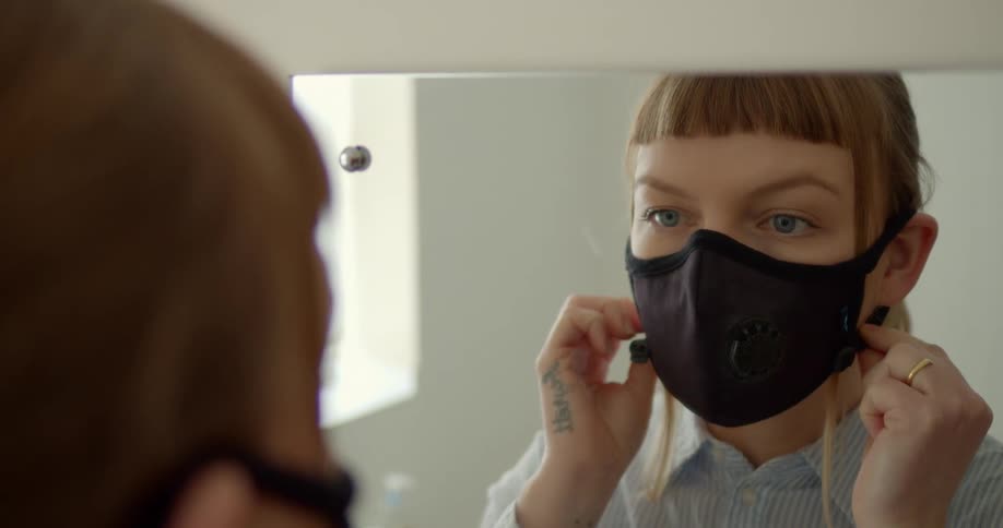 A woman looking into a mirror and putting on a mask
