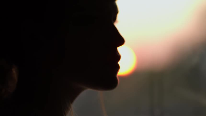 A silhouette of a womans face with the sun shining through the window
