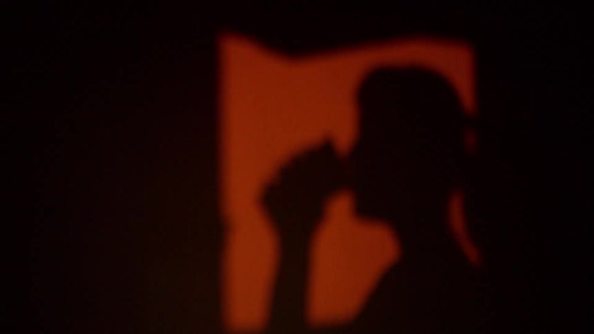 Shadow of woman cast onto wall as she stands near opening and drinks