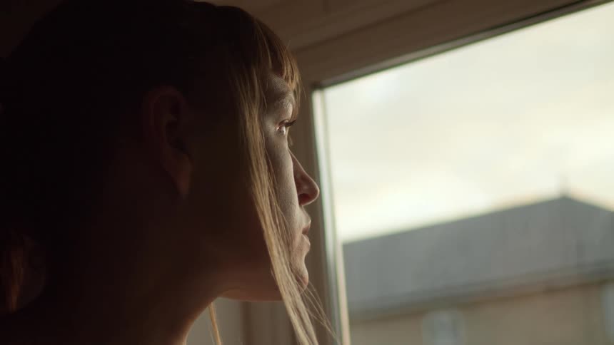 Woman stands near window looking out
