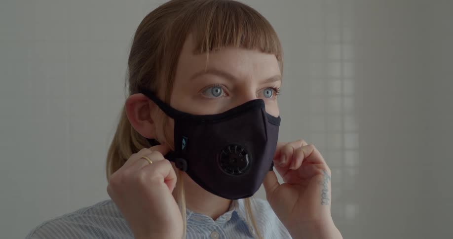 Close up of woman standing in a room adjusting her face mask