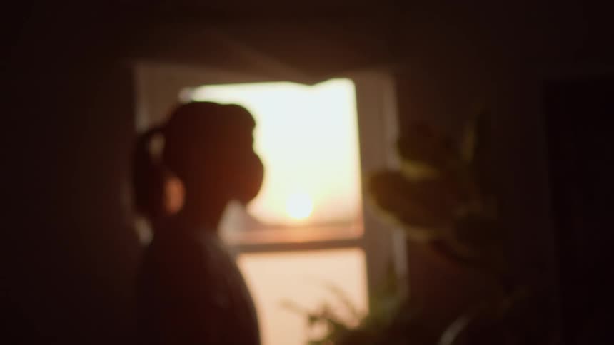 Silhouette of woman wearing face mask in front of window at sunset