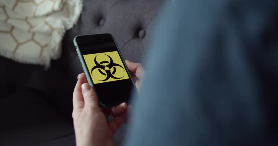 A person sitting on a couch holding a smart phone with a biohazard symbol