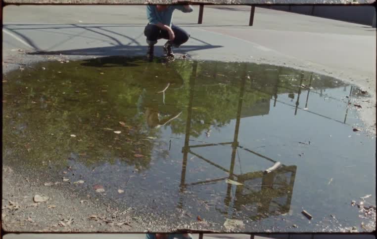 Woman crouches down and looks at her reflection on the surface of a puddle
