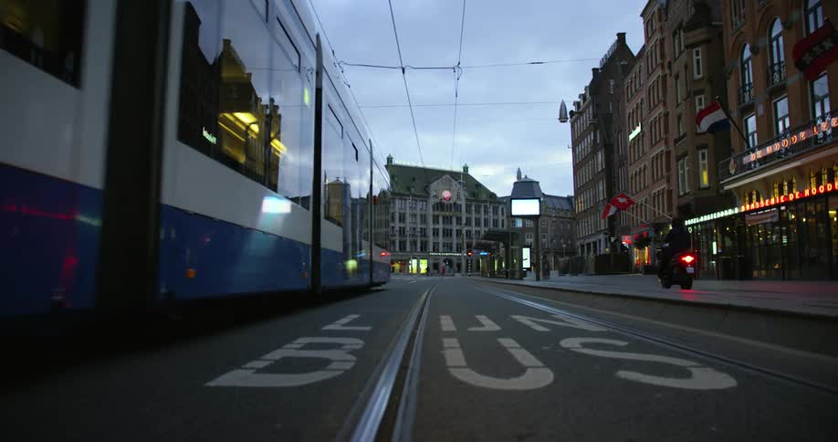 A subway goes down a city street as people walk along and a motorcycle drives by