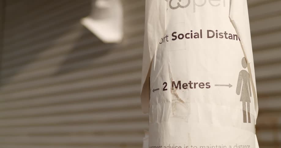 Paper sign advising social distancing tacked up on pole