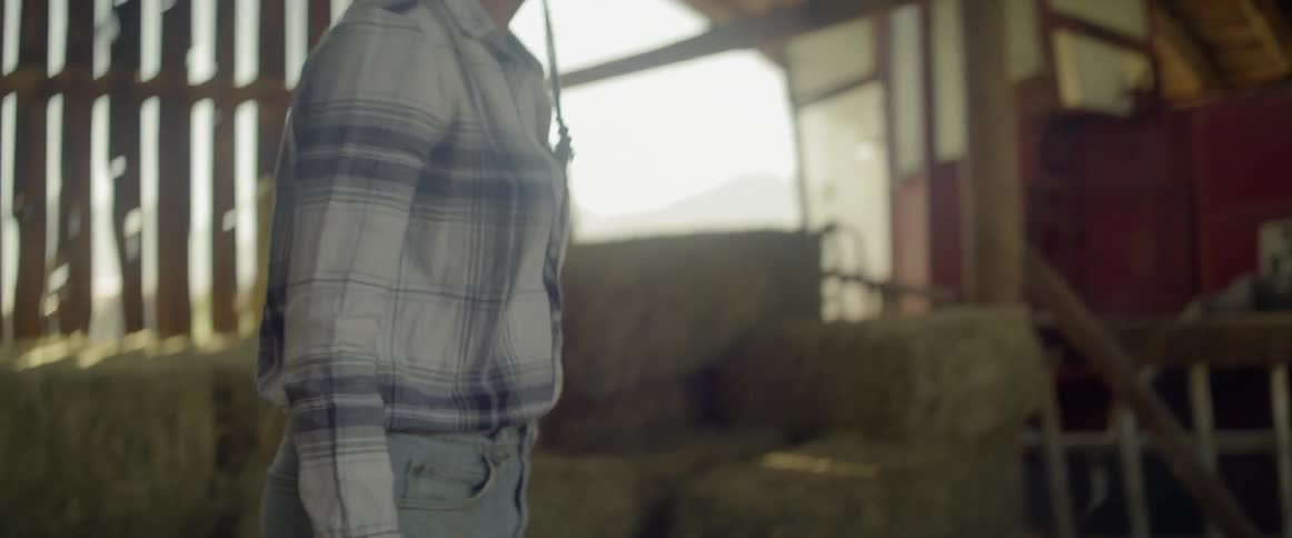 A woman lifts a hay bale and moves it across the barn
