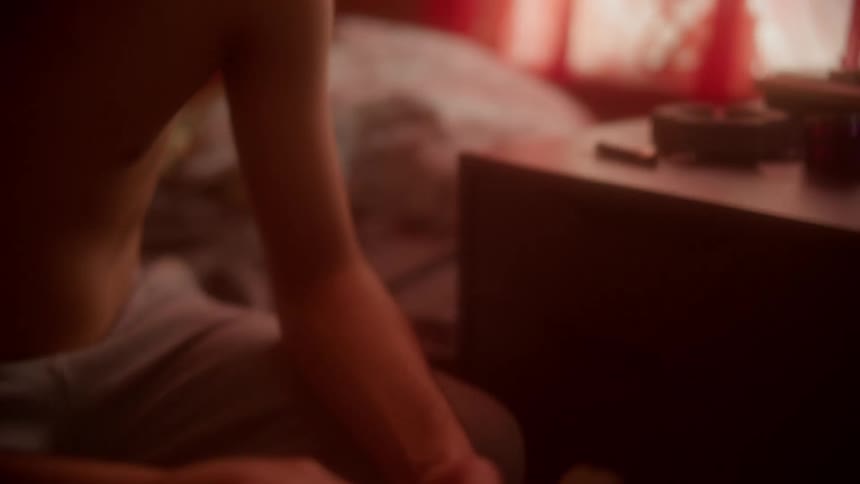 A man sitting on a bed takes a marijuana joint and lights it with a lighter