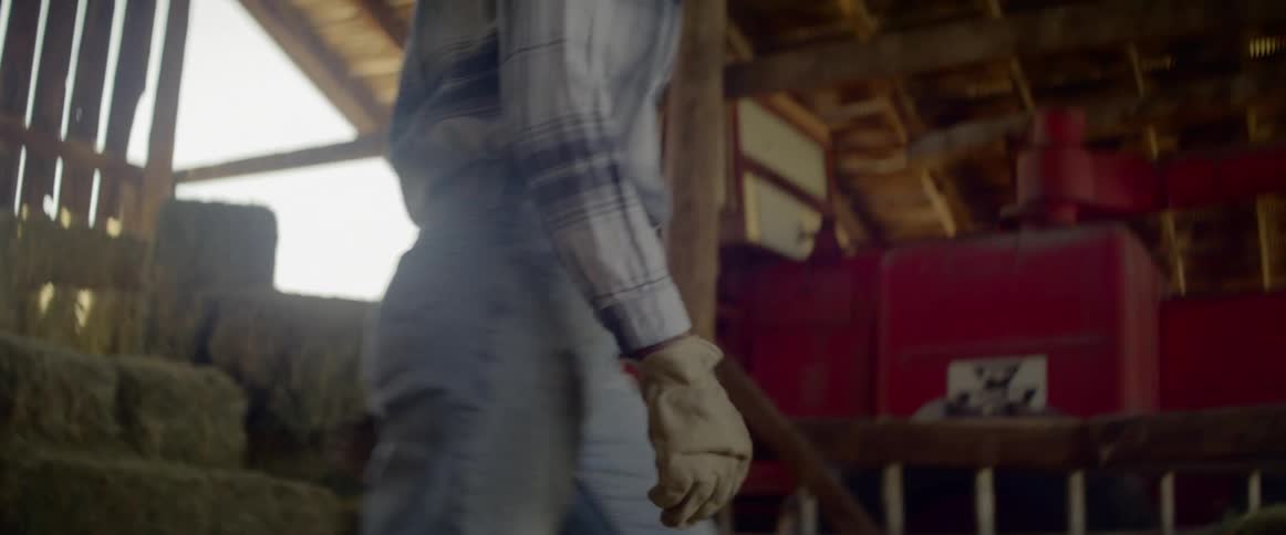 Woman lifts up and carries a bale of hay in the barn