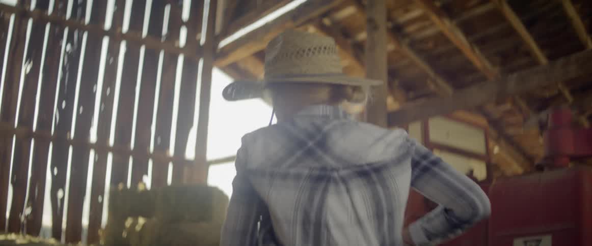 A woman with gloves picking up and moving a bale of hay