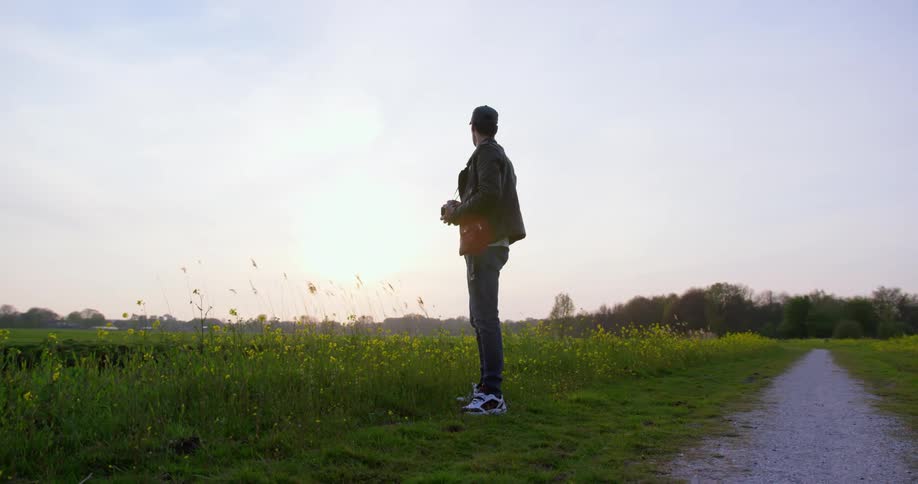 A man with a camera stands in a field near a gravel path