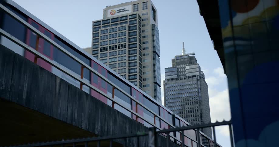 A subway train travels on an elevated track through a city and over a building with a colorful mural