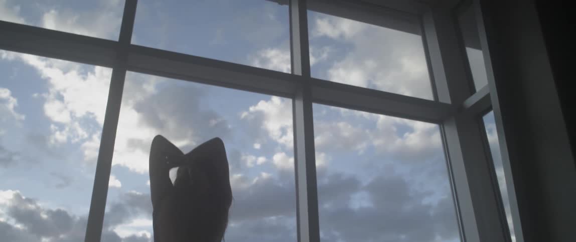 A woman stretches in front of windows on a cloudy day