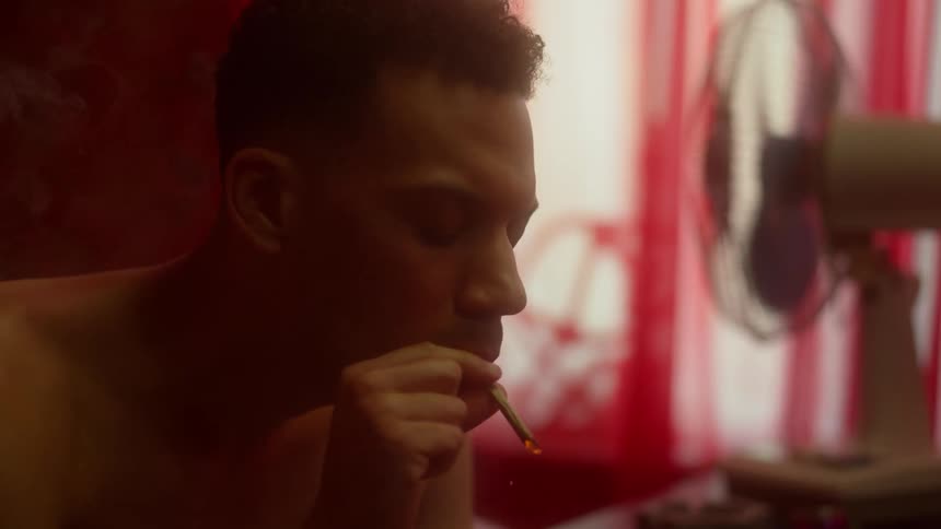 Shirtless black man lights a cigarette in his room