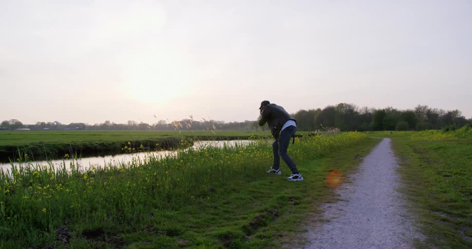 A man leans down to take a photo of flowers in a field near a forest