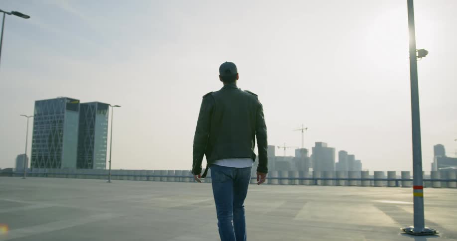 Man walks across empty parking lot with city skyline on the horizon