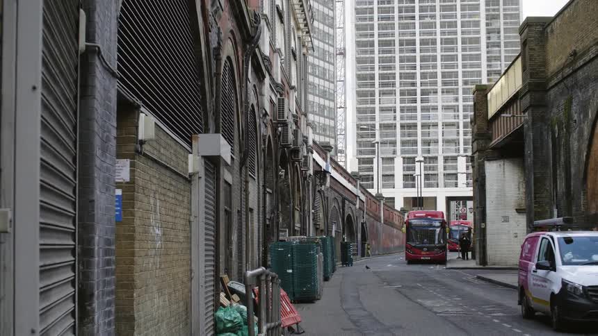 A bus and commercial van parked in an alley lined with closed and gated stores and shops